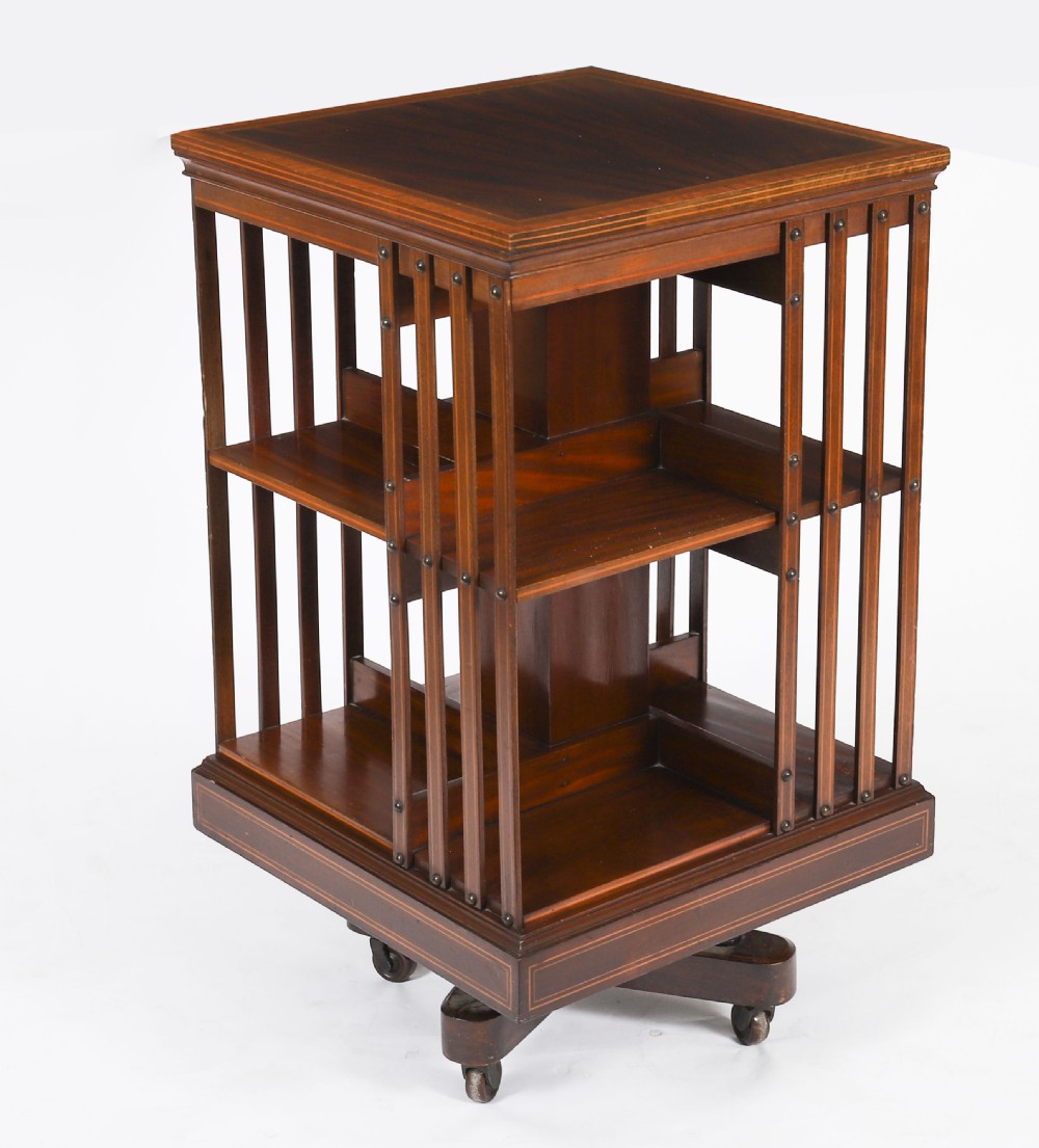 An Edwardian flame mahogany two-tier revolving bookcase featuring satinwood crossbanding, slatted sides with brass studs, and a rotating base on castors. View II