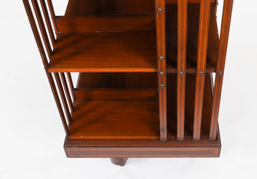 An Edwardian flame mahogany two-tier revolving bookcase featuring satinwood crossbanding, slatted sides with brass studs, and a rotating base on castors. View VI
