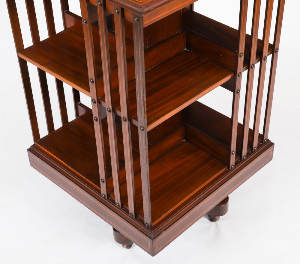 An Edwardian flame mahogany two-tier revolving bookcase featuring satinwood crossbanding, slatted sides with brass studs, and a rotating base on castors. View VII