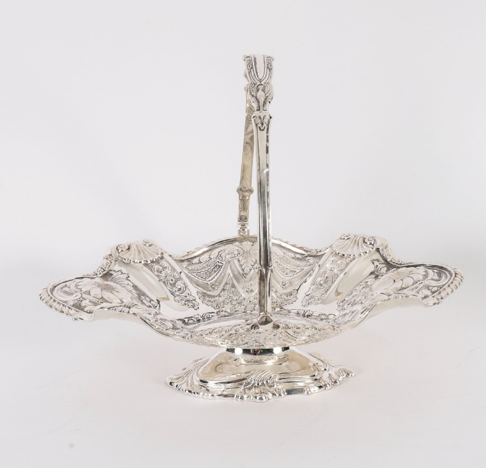 An ornate Victorian silver-plated fruit basket featuring chased floral motifs, a scalloped shell rim, a pedestal base, and a hinged overhead swing handle. View III