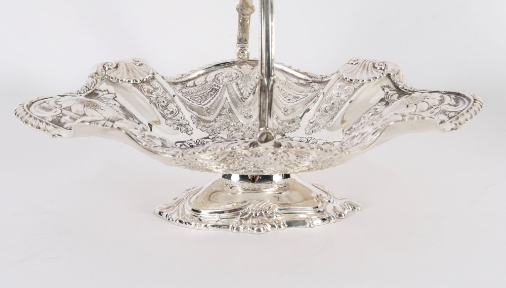 An ornate Victorian silver-plated fruit basket featuring chased floral motifs, a scalloped shell rim, a pedestal base, and a hinged overhead swing handle. View IV