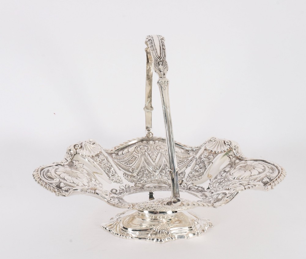 An ornate Victorian silver-plated fruit basket featuring chased floral motifs, a scalloped shell rim, a pedestal base, and a hinged overhead swing handle. View VII