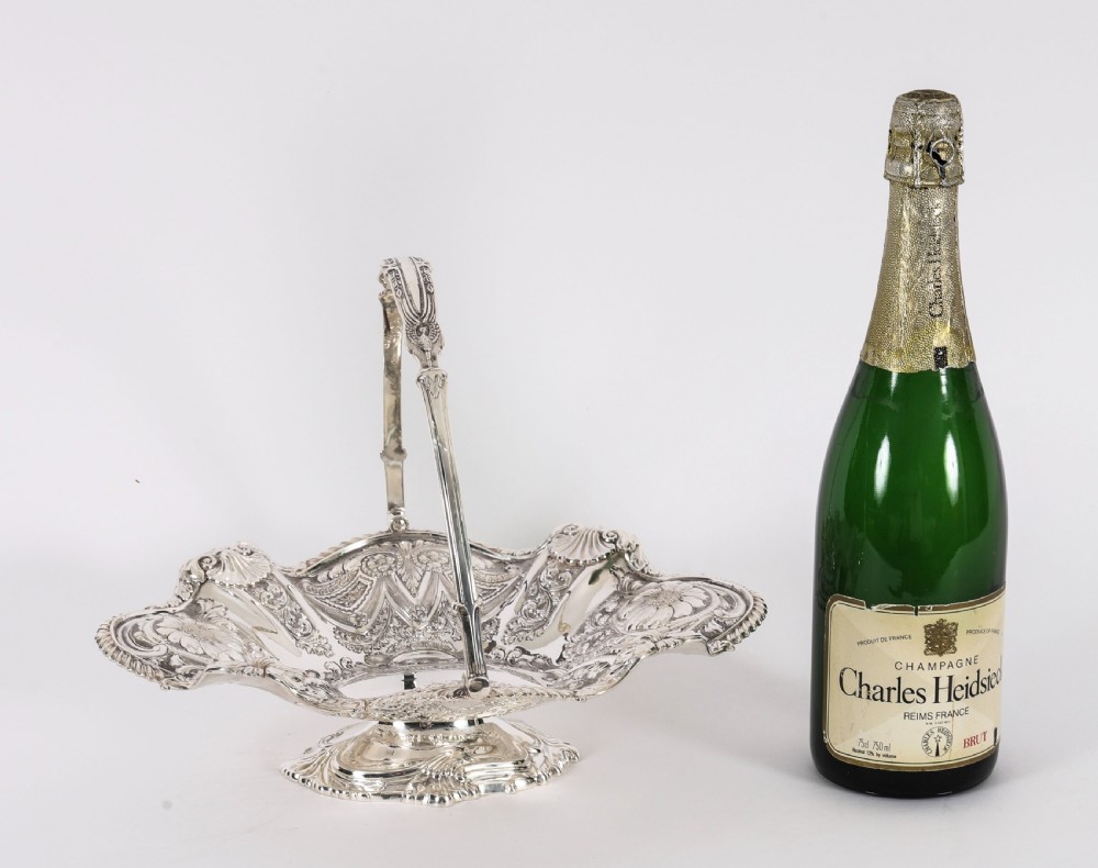 An ornate Victorian silver-plated fruit basket featuring chased floral motifs, a scalloped shell rim, a pedestal base, and a hinged overhead swing handle. View VIII