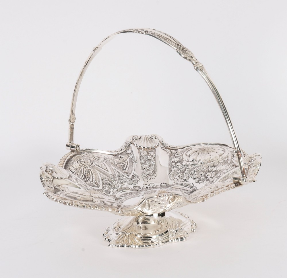 An ornate Victorian silver-plated fruit basket featuring chased floral motifs, a scalloped shell rim, a pedestal base, and a hinged overhead swing handle. View XV