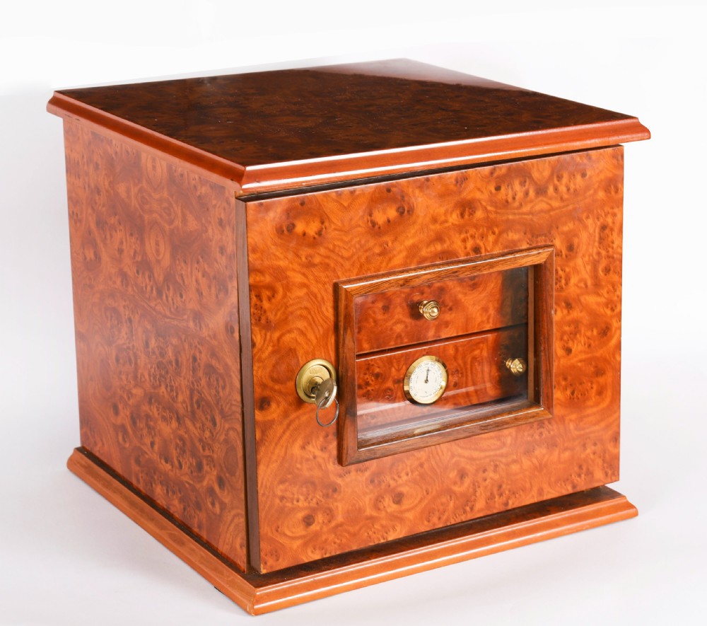 A square burr elm cigar humidor cabinet featuring a glass viewing window, brass hygrometer, front lock, and polished wood figure.
