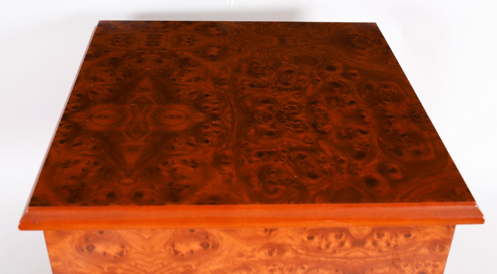 A square burr elm cigar humidor cabinet featuring a glass viewing window, brass hygrometer, front lock, and polished wood figure. View V