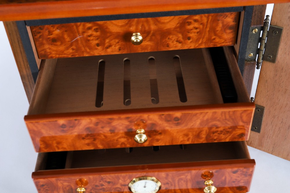 A square burr elm cigar humidor cabinet featuring a glass viewing window, brass hygrometer, front lock, and polished wood figure. View VII