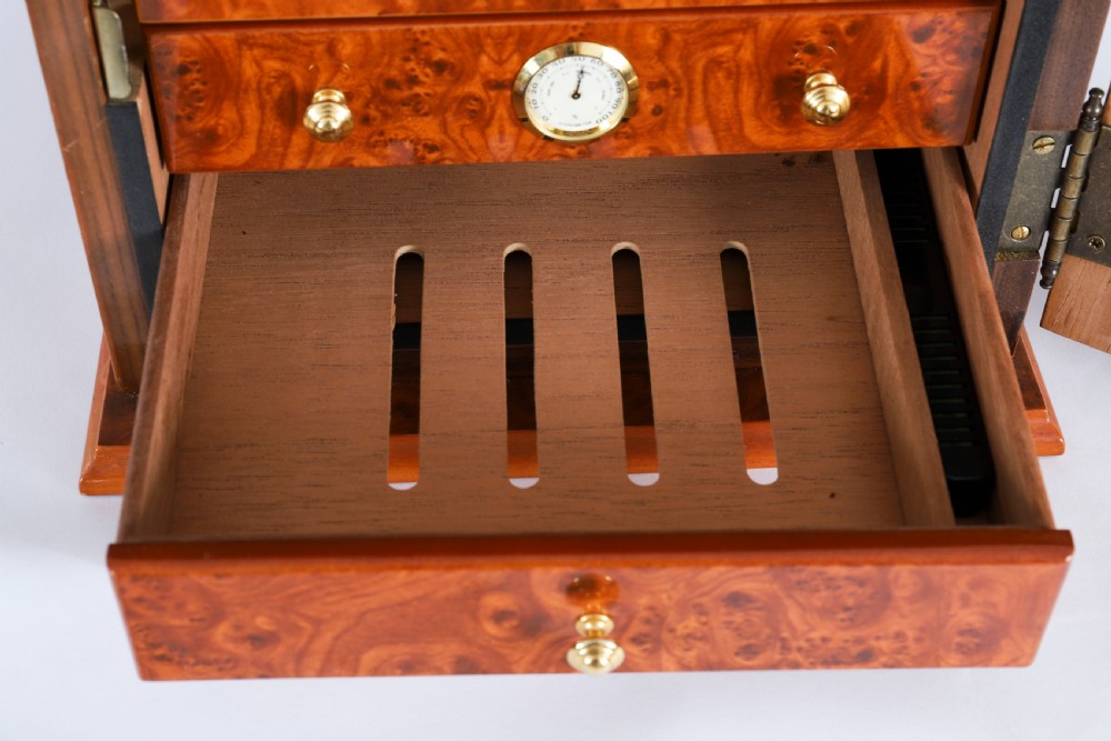 A square burr elm cigar humidor cabinet featuring a glass viewing window, brass hygrometer, front lock, and polished wood figure. View IX