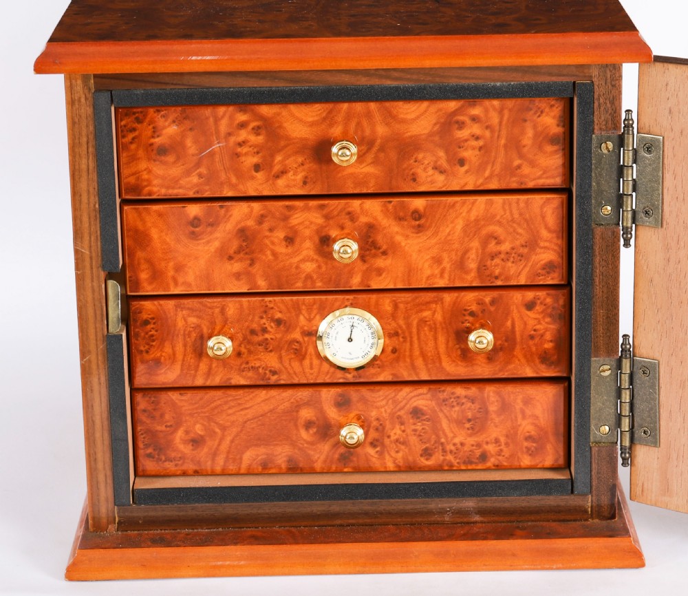 A square burr elm cigar humidor cabinet featuring a glass viewing window, brass hygrometer, front lock, and polished wood figure. View X