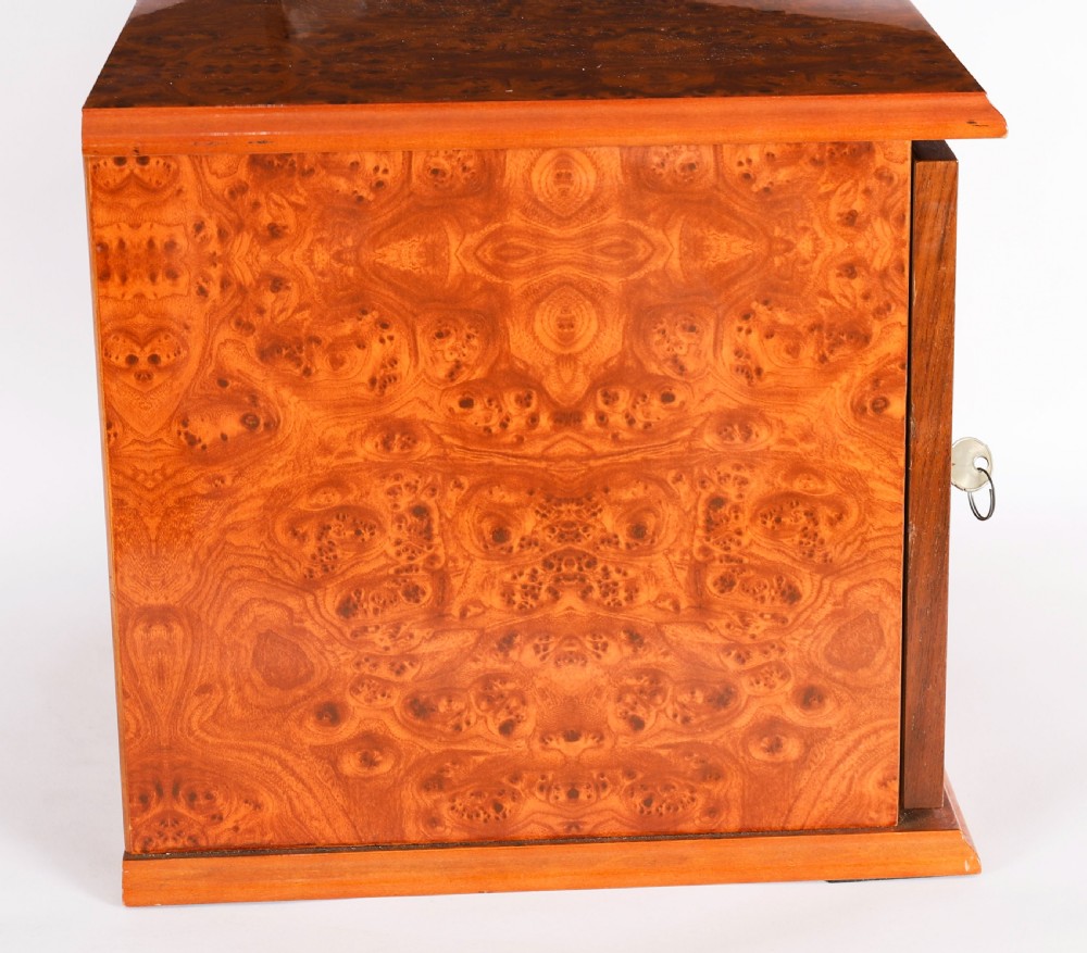 A square burr elm cigar humidor cabinet featuring a glass viewing window, brass hygrometer, front lock, and polished wood figure. View XIV