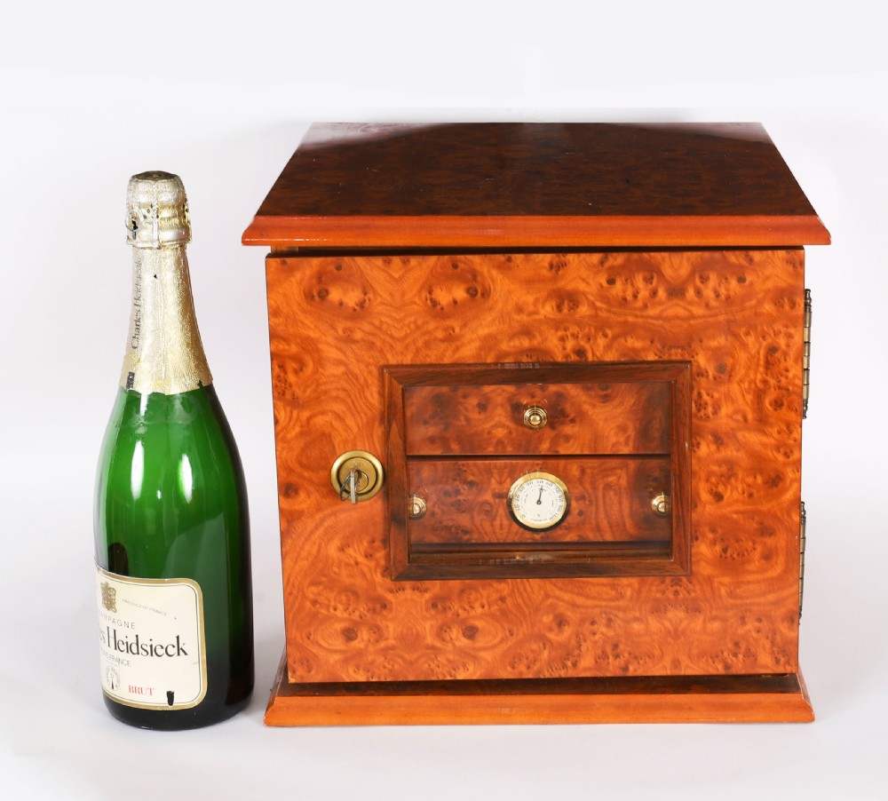 A square burr elm cigar humidor cabinet featuring a glass viewing window, brass hygrometer, front lock, and polished wood figure. View XVI
