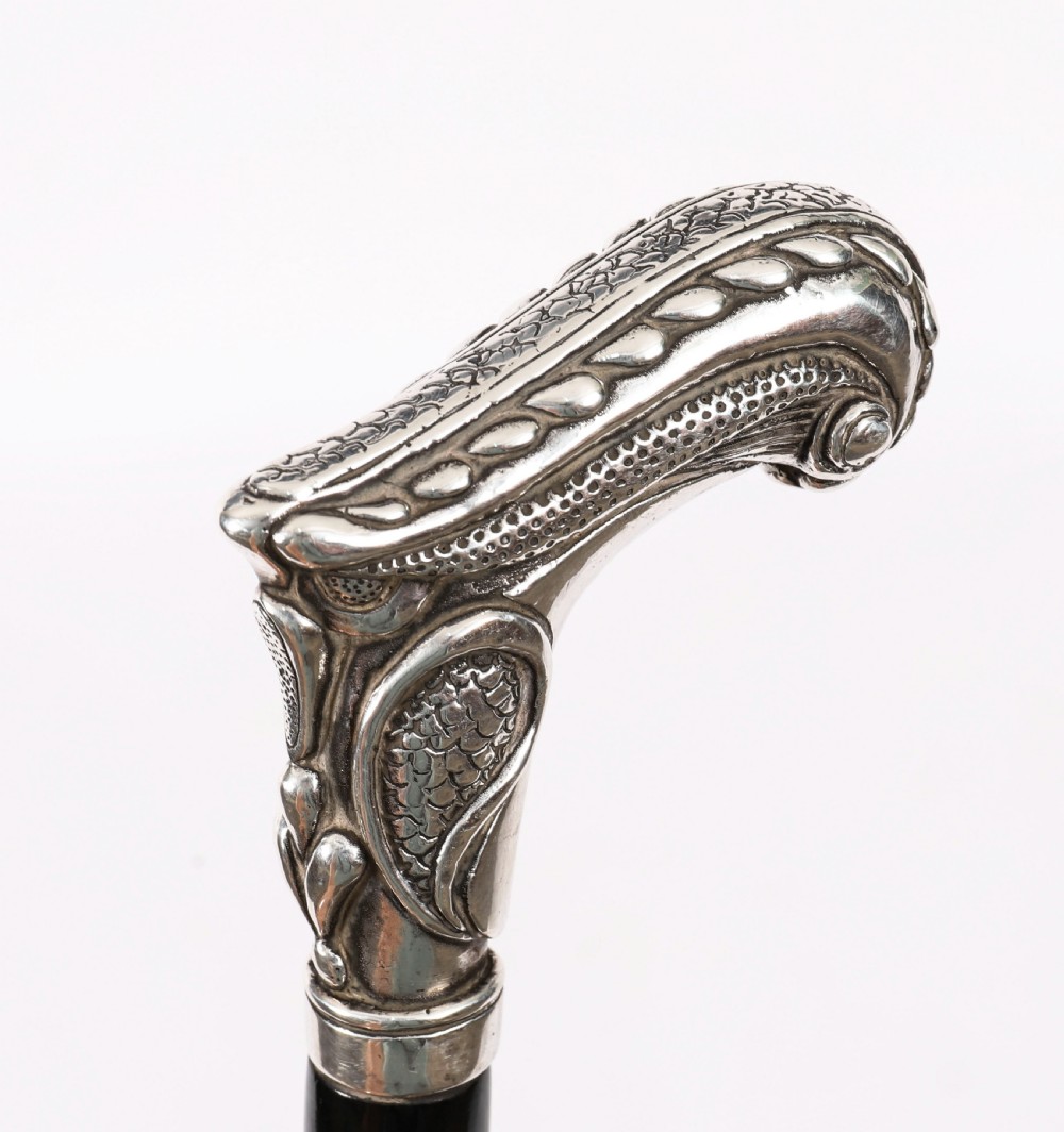 An antique French Art Nouveau walking cane featuring an ornate silver handle and a tapered black wooden shaft. View IV