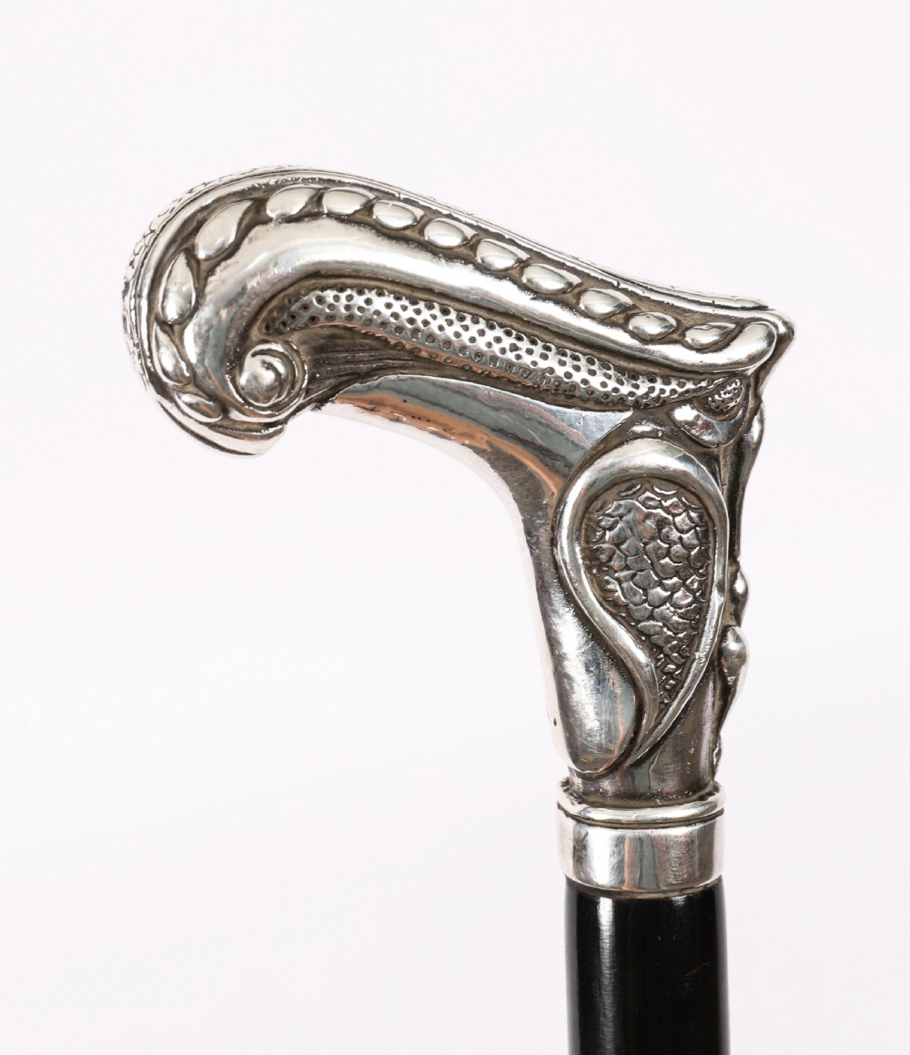 An antique French Art Nouveau walking cane featuring an ornate silver handle and a tapered black wooden shaft. View VI