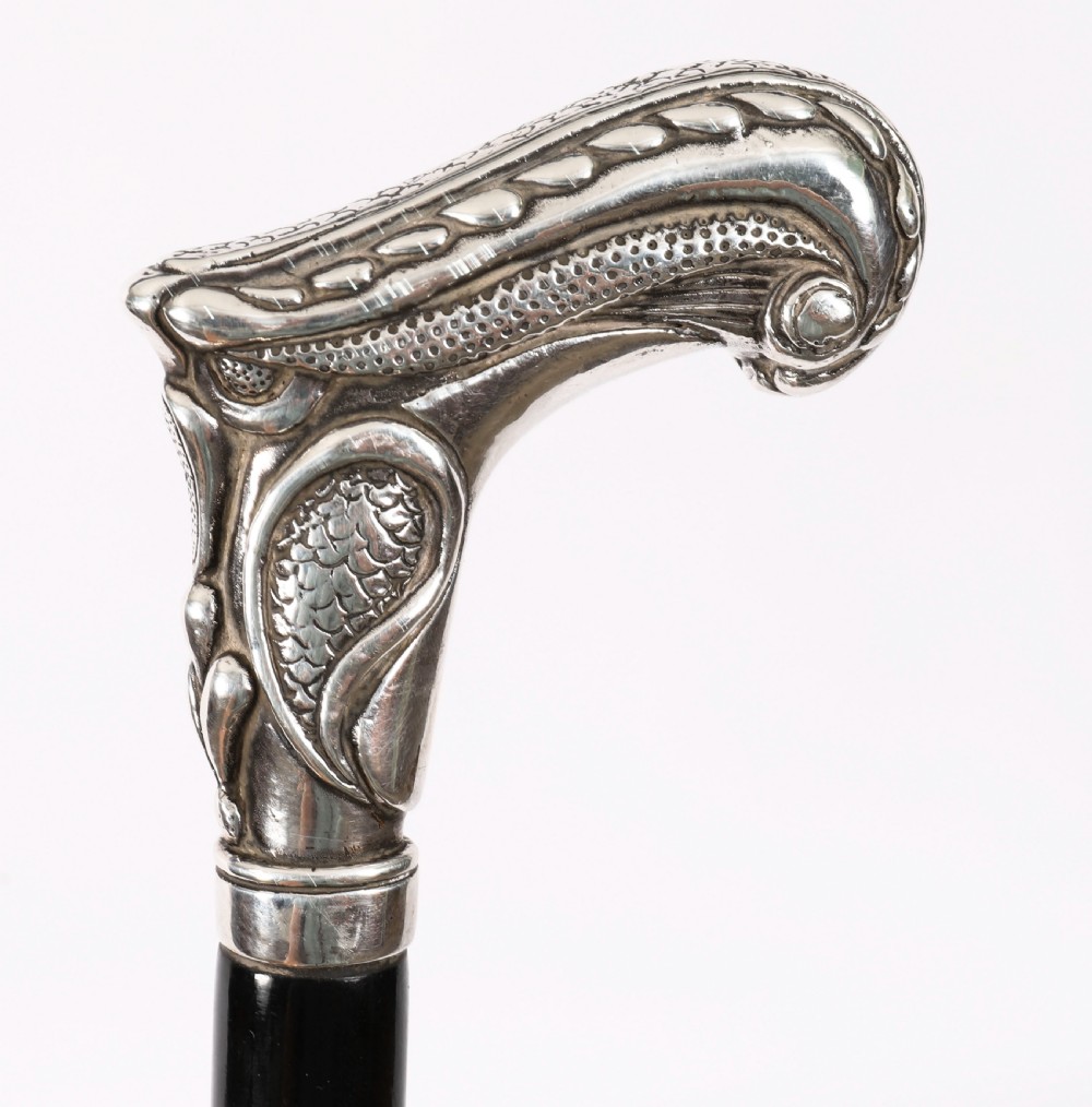 An antique French Art Nouveau walking cane featuring an ornate silver handle and a tapered black wooden shaft. View XII