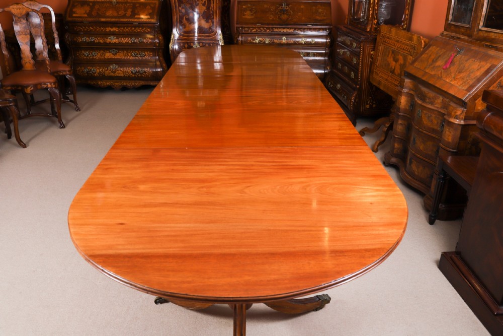 A long polished mahogany triple pillar dining table featuring splayed tripod bases fitted with brass claw feet and castors. View V
