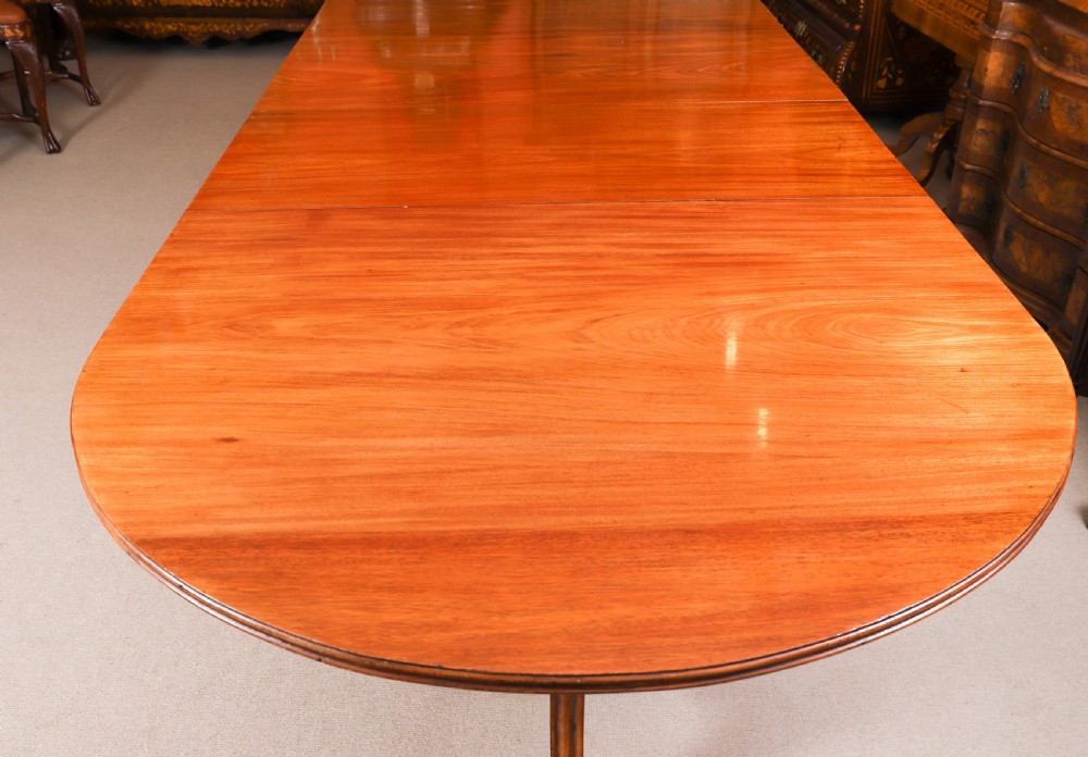 A long polished mahogany triple pillar dining table featuring splayed tripod bases fitted with brass claw feet and castors. View VI