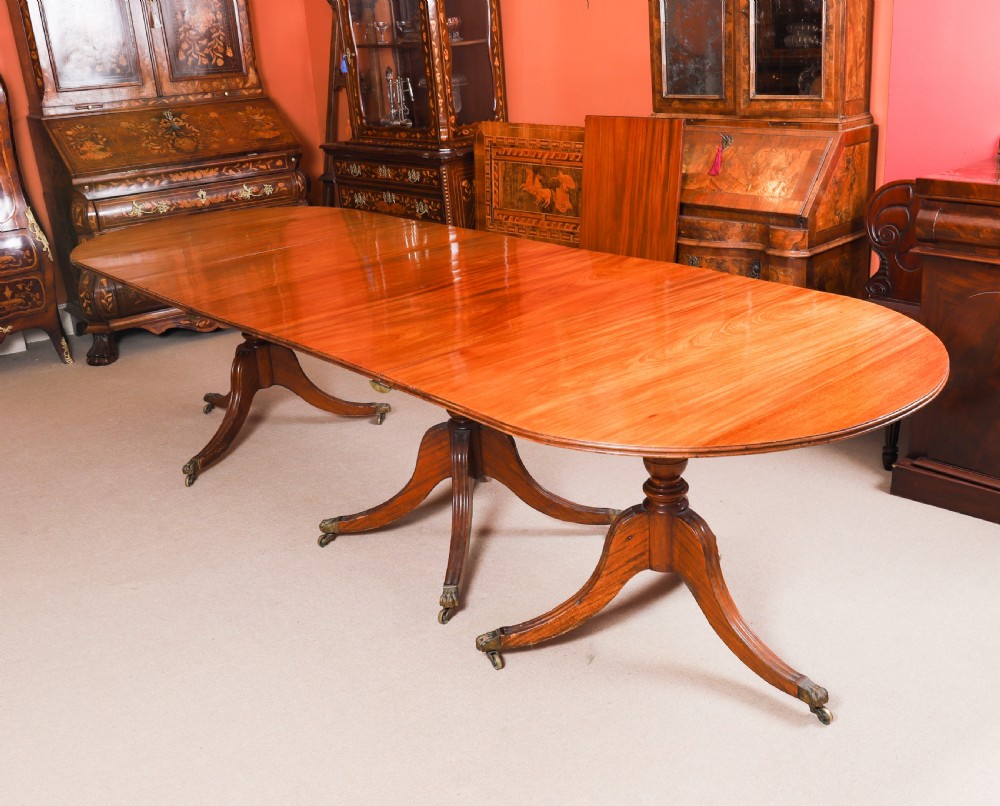A long polished mahogany triple pillar dining table featuring splayed tripod bases fitted with brass claw feet and castors. View X