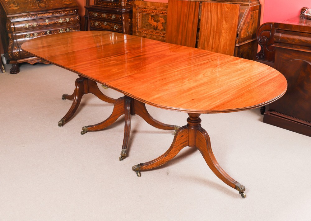 A long polished mahogany triple pillar dining table featuring splayed tripod bases fitted with brass claw feet and castors. View XI