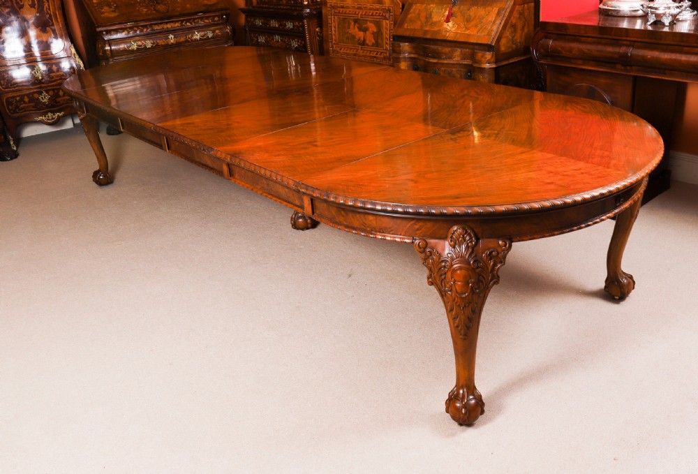 A large 19th-century burr walnut extending dining table with figured grain patterns, carved cabriole legs, and ball-and-claw feet.