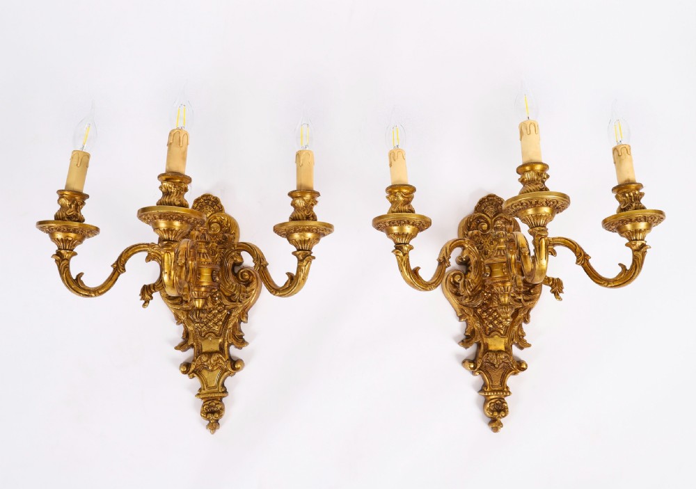 A pair of French gilt bronze three-arm wall sconces featuring scrolled foliate ornamentation and decorative backplates.