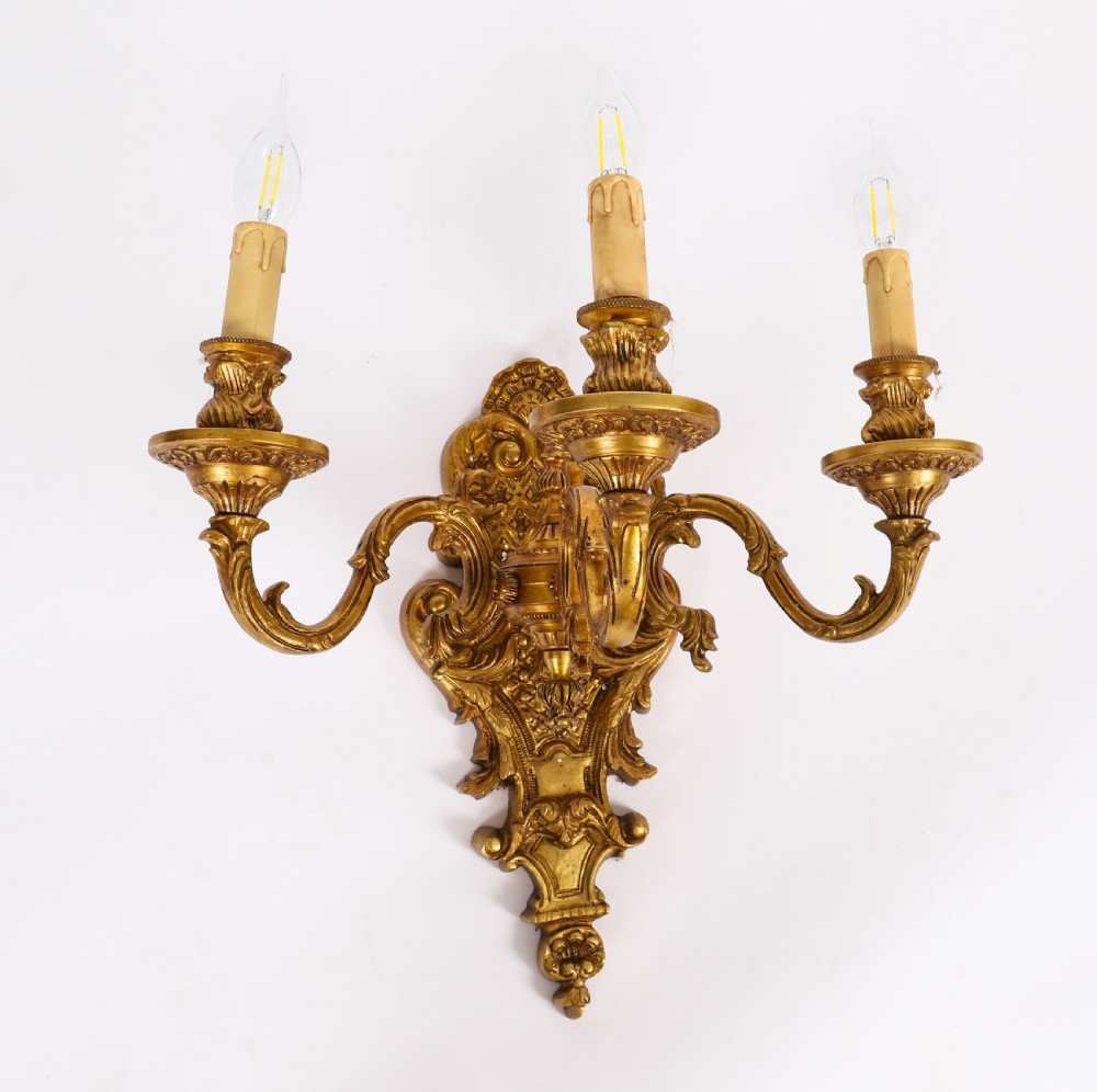 A pair of French gilt bronze three-arm wall sconces featuring scrolled foliate ornamentation and decorative backplates. View II