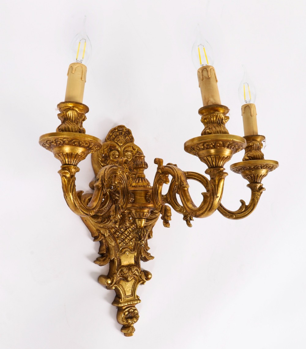 A pair of French gilt bronze three-arm wall sconces featuring scrolled foliate ornamentation and decorative backplates. View V