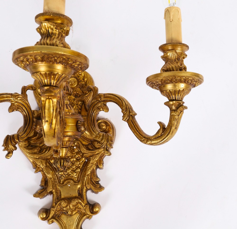 A pair of French gilt bronze three-arm wall sconces featuring scrolled foliate ornamentation and decorative backplates. View X
