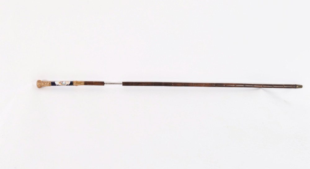 A nineteenth-century French walking cane featuring a dark wooden shaft, a concealed steel blade, and a gilt metal handle mounted with painted Sevres porcelain.