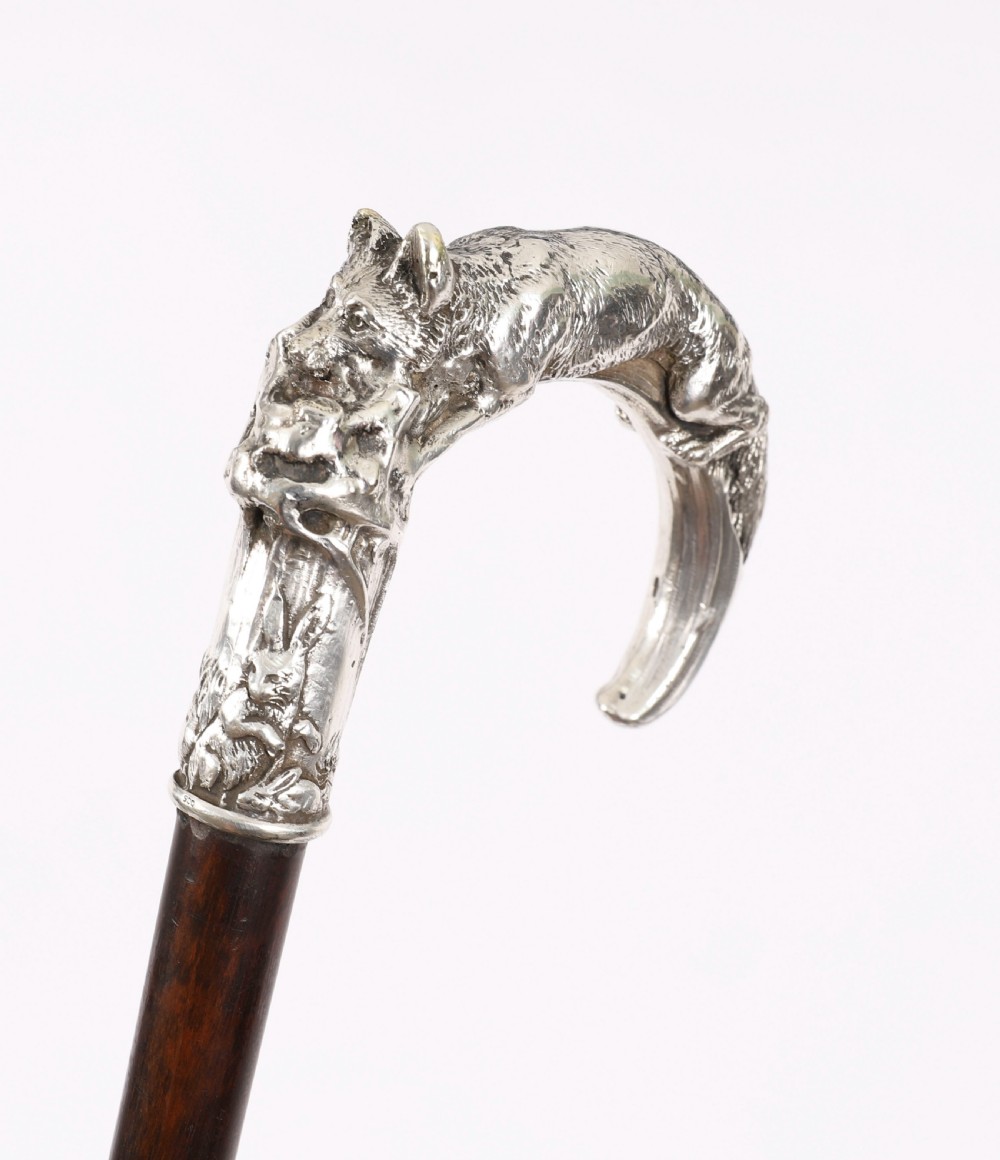 An antique walking stick featuring a detailed silver handle depicting a fox and hare, set atop a dark wood shaft with a metal ferrule. View II
