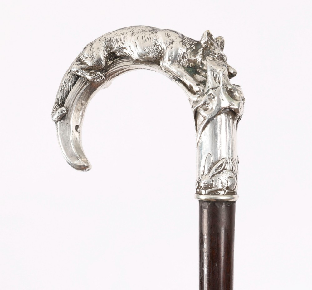 An antique walking stick featuring a detailed silver handle depicting a fox and hare, set atop a dark wood shaft with a metal ferrule. View XVIII