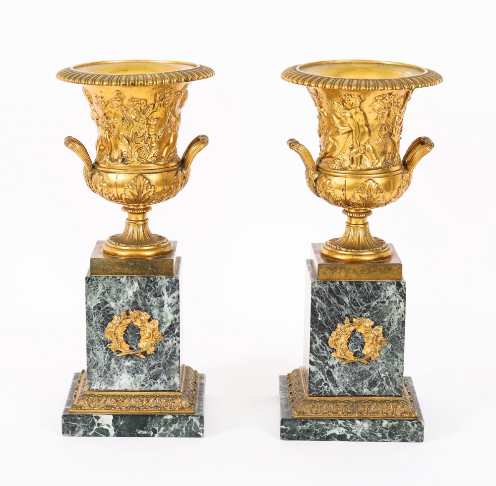 A pair of 19th-century French Grand Tour gilt bronze campana urns featuring classical figure reliefs, mounted on square green marble pedestal bases with gilt laurel wreaths.