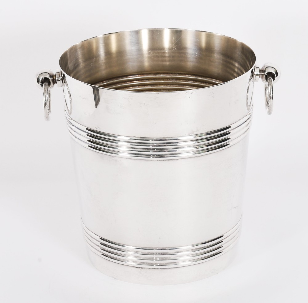 An Art Deco silver-plated champagne cooler featuring reeded horizontal bands and twin drop-ring handles on spherical mounts.