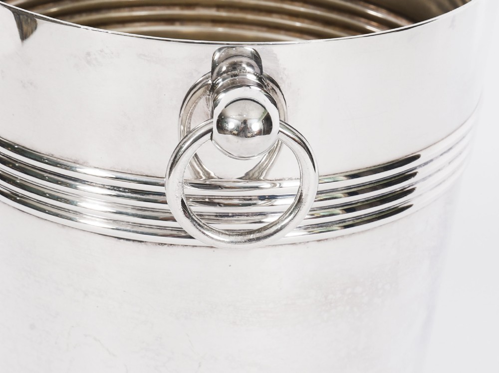 An Art Deco silver-plated champagne cooler featuring reeded horizontal bands and twin drop-ring handles on spherical mounts. View IX