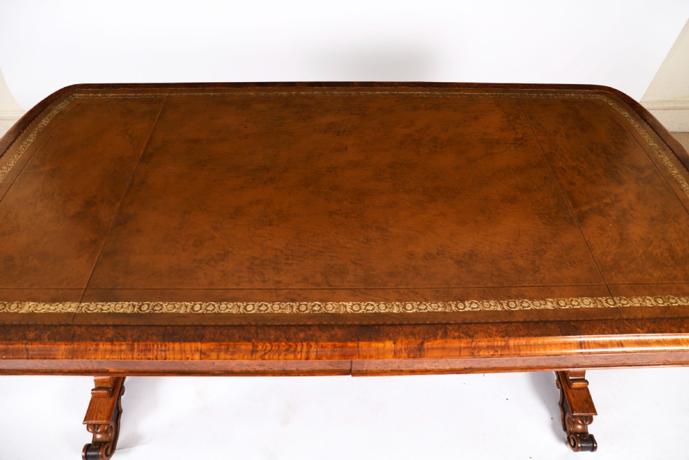 A 19th-century Victorian pollard oak writing table featuring a brown leather inset top, carved trestle end supports, a turned central stretcher, and scroll feet on brass castors. View V