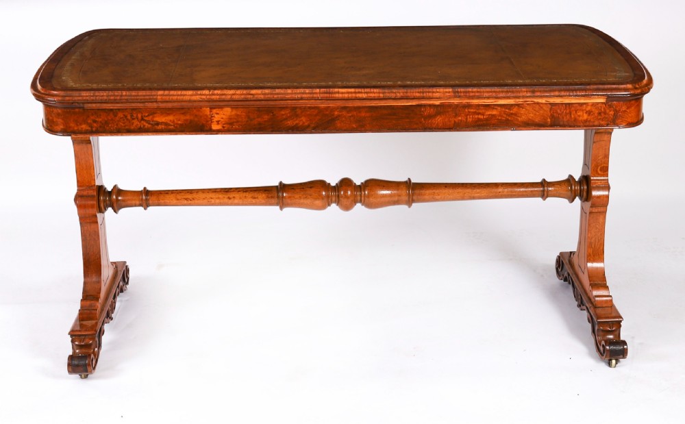 A 19th-century Victorian pollard oak writing table featuring a brown leather inset top, carved trestle end supports, a turned central stretcher, and scroll feet on brass castors. View VIII