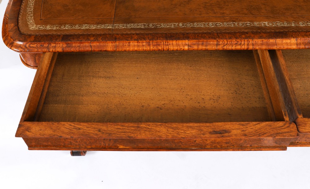 A 19th-century Victorian pollard oak writing table featuring a brown leather inset top, carved trestle end supports, a turned central stretcher, and scroll feet on brass castors. View XIV