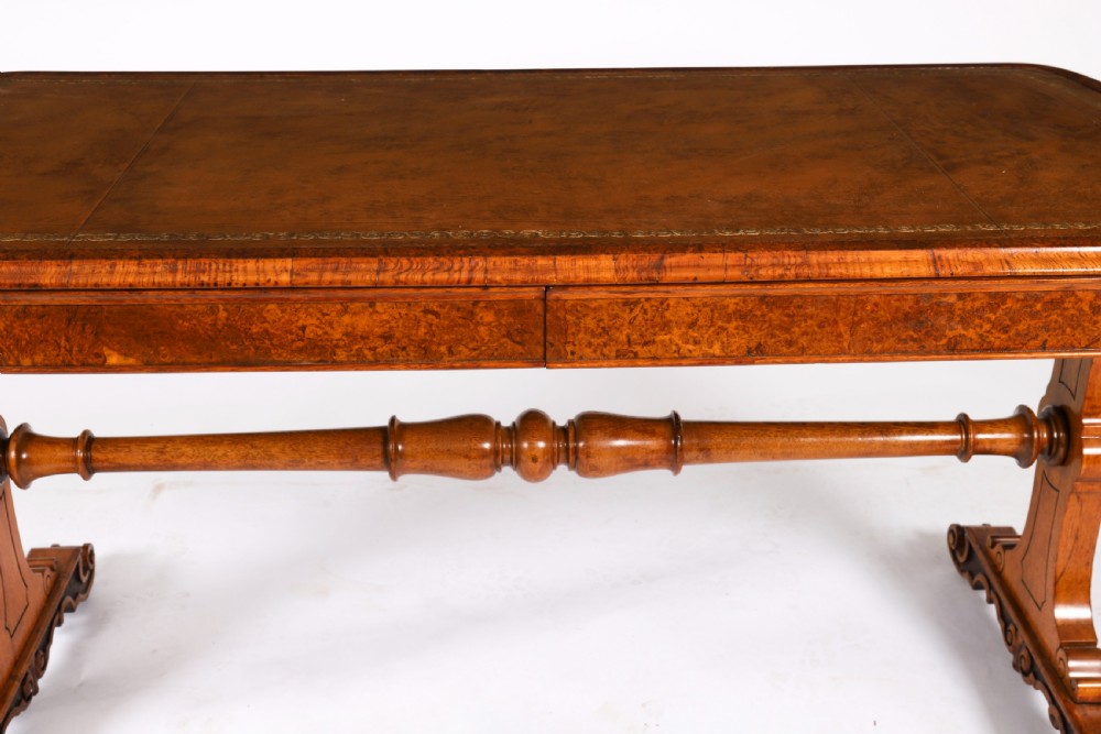 A 19th-century Victorian pollard oak writing table featuring a brown leather inset top, carved trestle end supports, a turned central stretcher, and scroll feet on brass castors. View XV