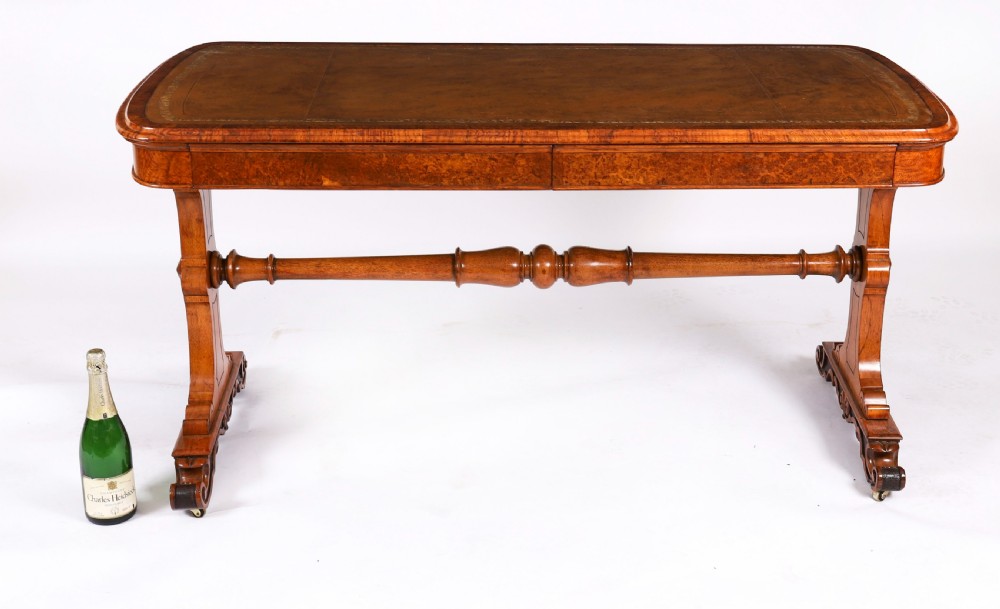 A 19th-century Victorian pollard oak writing table featuring a brown leather inset top, carved trestle end supports, a turned central stretcher, and scroll feet on brass castors. View XVI