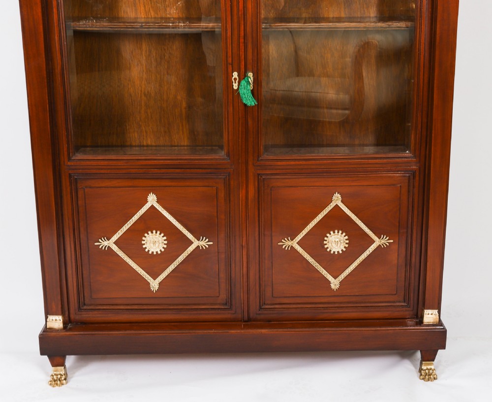 A nineteenth-century French Empire Revival mahogany bookcase featuring twin glazed doors, gilt bronze mounts, a marble top, and metal paw feet. View VI