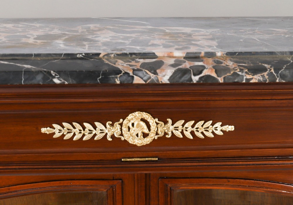 A nineteenth-century French Empire Revival mahogany bookcase featuring twin glazed doors, gilt bronze mounts, a marble top, and metal paw feet. View XI