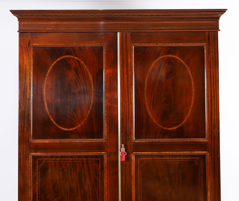 A late 19th-century George III revival flame mahogany double wardrobe featuring oval panel inlays, twin doors, a single bottom drawer, and a moulded cornice. View II