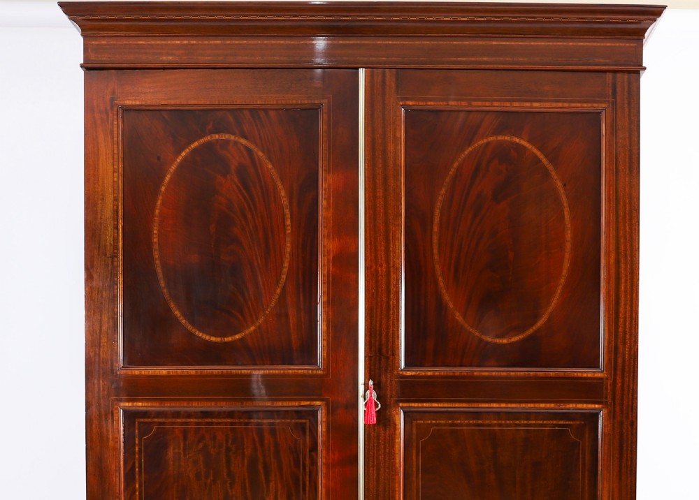 A late 19th-century George III revival flame mahogany double wardrobe featuring oval panel inlays, twin doors, a single bottom drawer, and a moulded cornice. View III