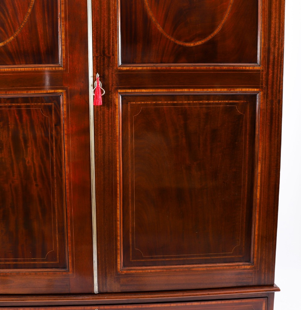 A late 19th-century George III revival flame mahogany double wardrobe featuring oval panel inlays, twin doors, a single bottom drawer, and a moulded cornice. View X