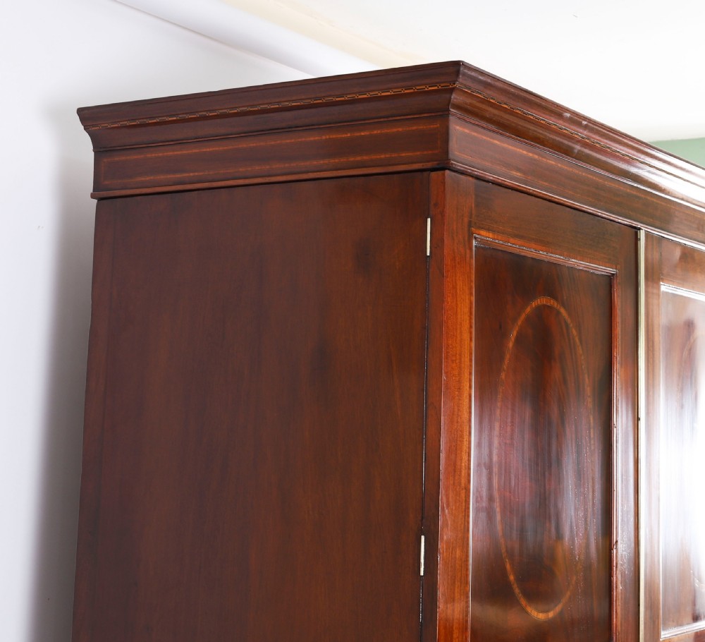 A late 19th-century George III revival flame mahogany double wardrobe featuring oval panel inlays, twin doors, a single bottom drawer, and a moulded cornice. View XVII