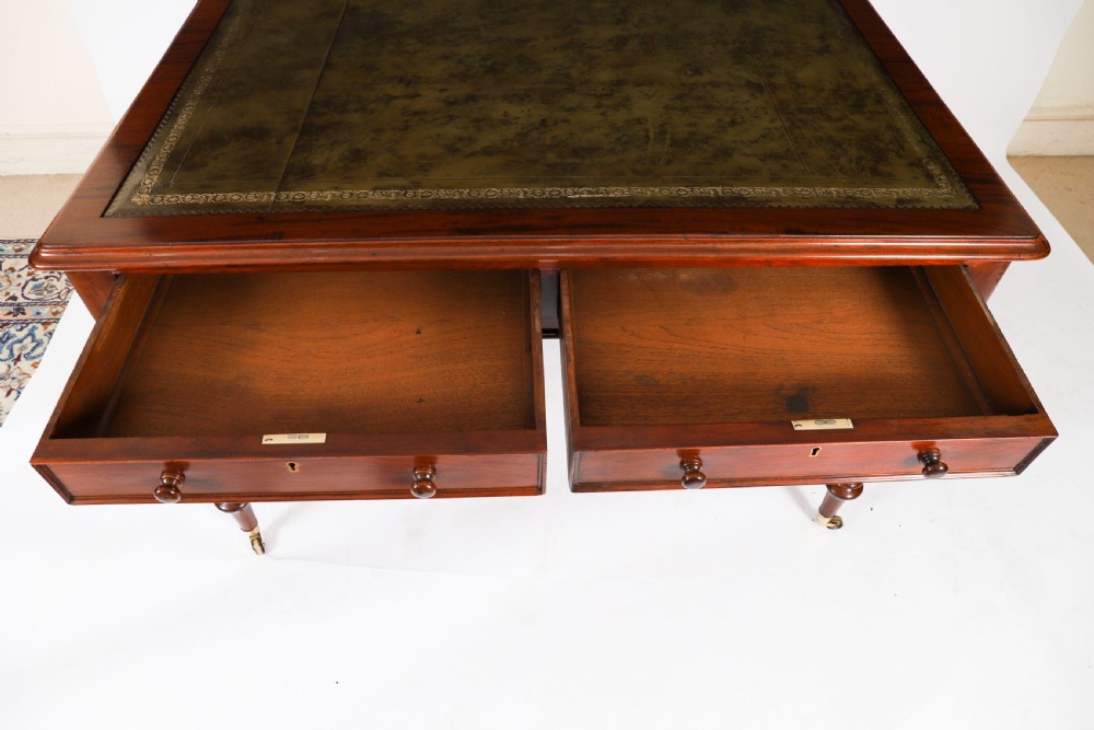 A nineteenth-century Victorian mahogany partners writing desk featuring a green leather inset top, frieze drawers with turned wood knob handles, and tapered legs on brass castors. View XIII