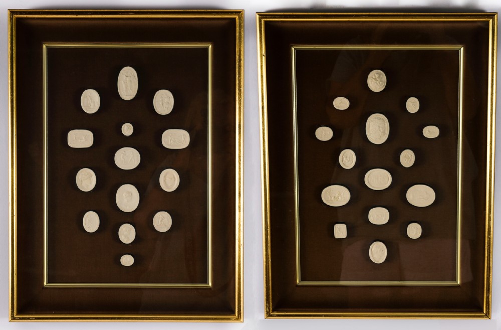 A pair of dark velvet-lined gilt frames containing arrangements of white plaster classical intaglio cameos.