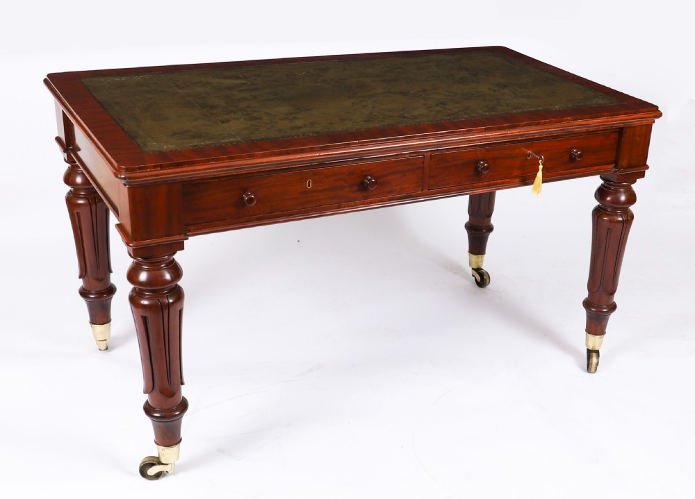 A William IV mahogany writing desk featuring an inset green leather surface, two frieze drawers with knob handles, turned fluted legs, and brass castors.