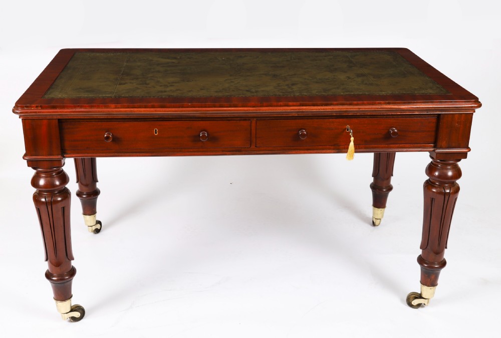 A William IV mahogany writing desk featuring an inset green leather surface, two frieze drawers with knob handles, turned fluted legs, and brass castors. View II