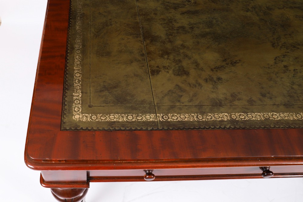 A William IV mahogany writing desk featuring an inset green leather surface, two frieze drawers with knob handles, turned fluted legs, and brass castors. View III