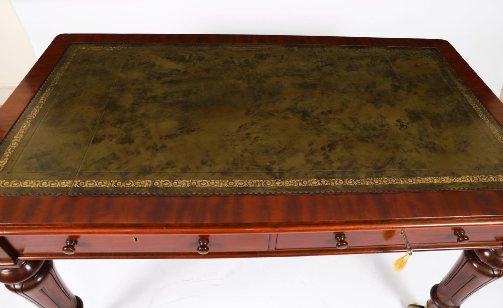 A William IV mahogany writing desk featuring an inset green leather surface, two frieze drawers with knob handles, turned fluted legs, and brass castors. View IV